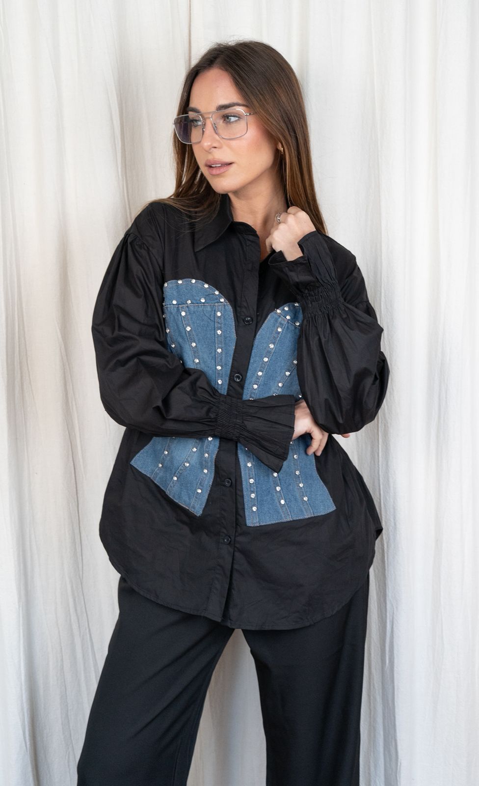 Mujer con camisa negra con panel vaquero y gafas, con la mano en la frente.