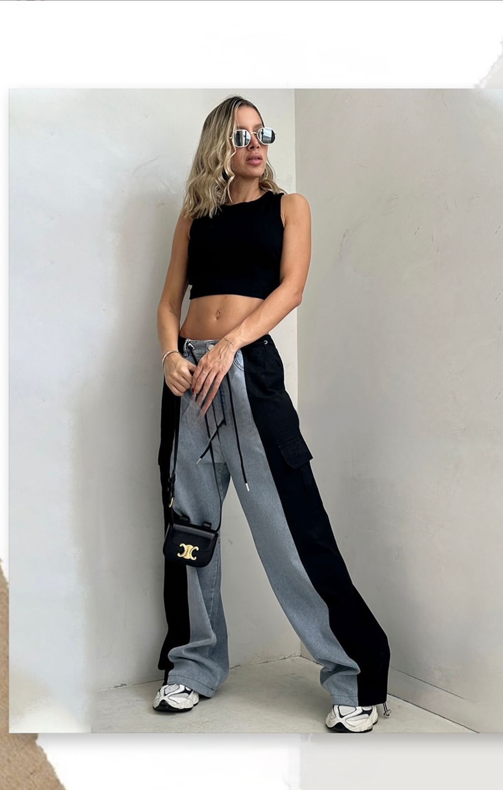 Mujer vestida con un top corto blanco y pantalones vaqueros bicolor, sosteniendo un pequeño bolso blanco