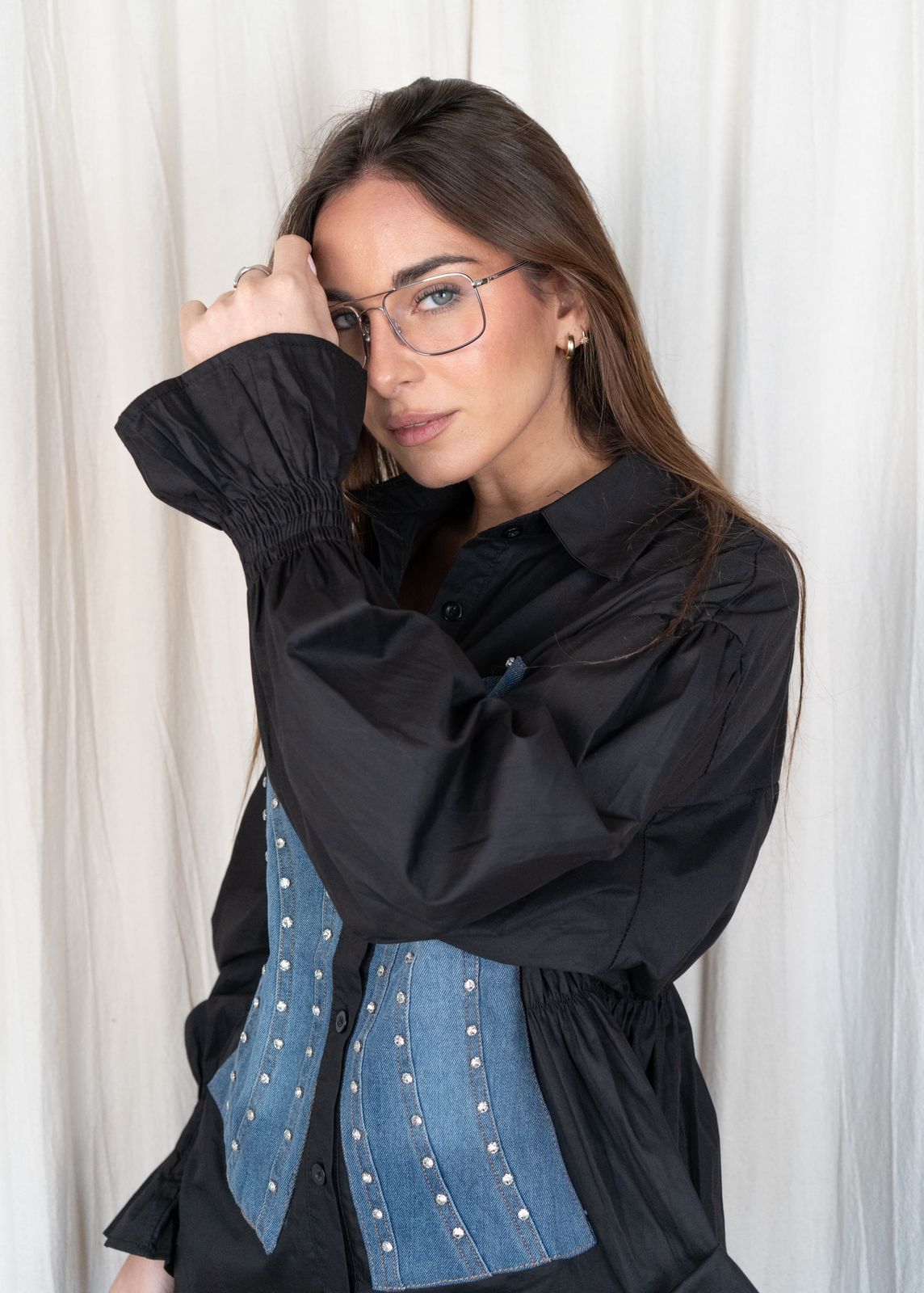 Mujer con camisa negra con panel vaquero y gafas, con la mano en la frente.