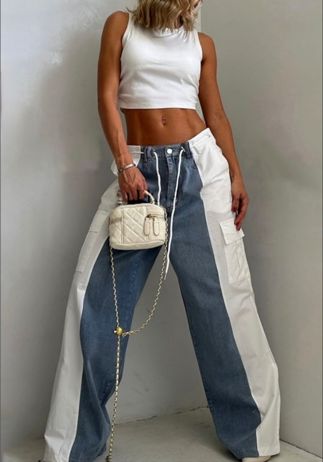 Mujer vestida con un top corto blanco y pantalones vaqueros bicolor, sosteniendo un pequeño bolso blanco