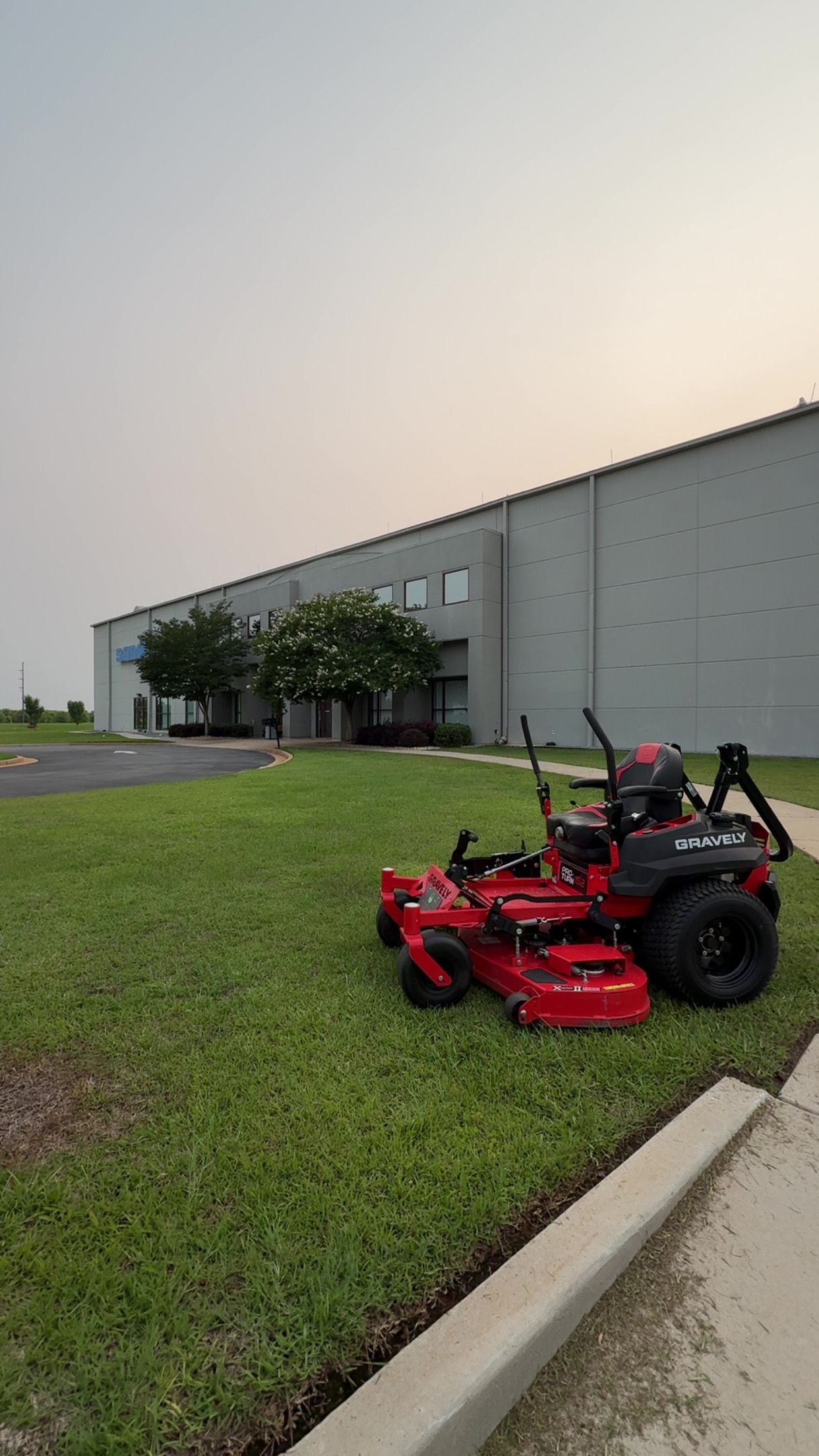 Red zero-turn lawnmower on grass near a building; the sky is overcast.