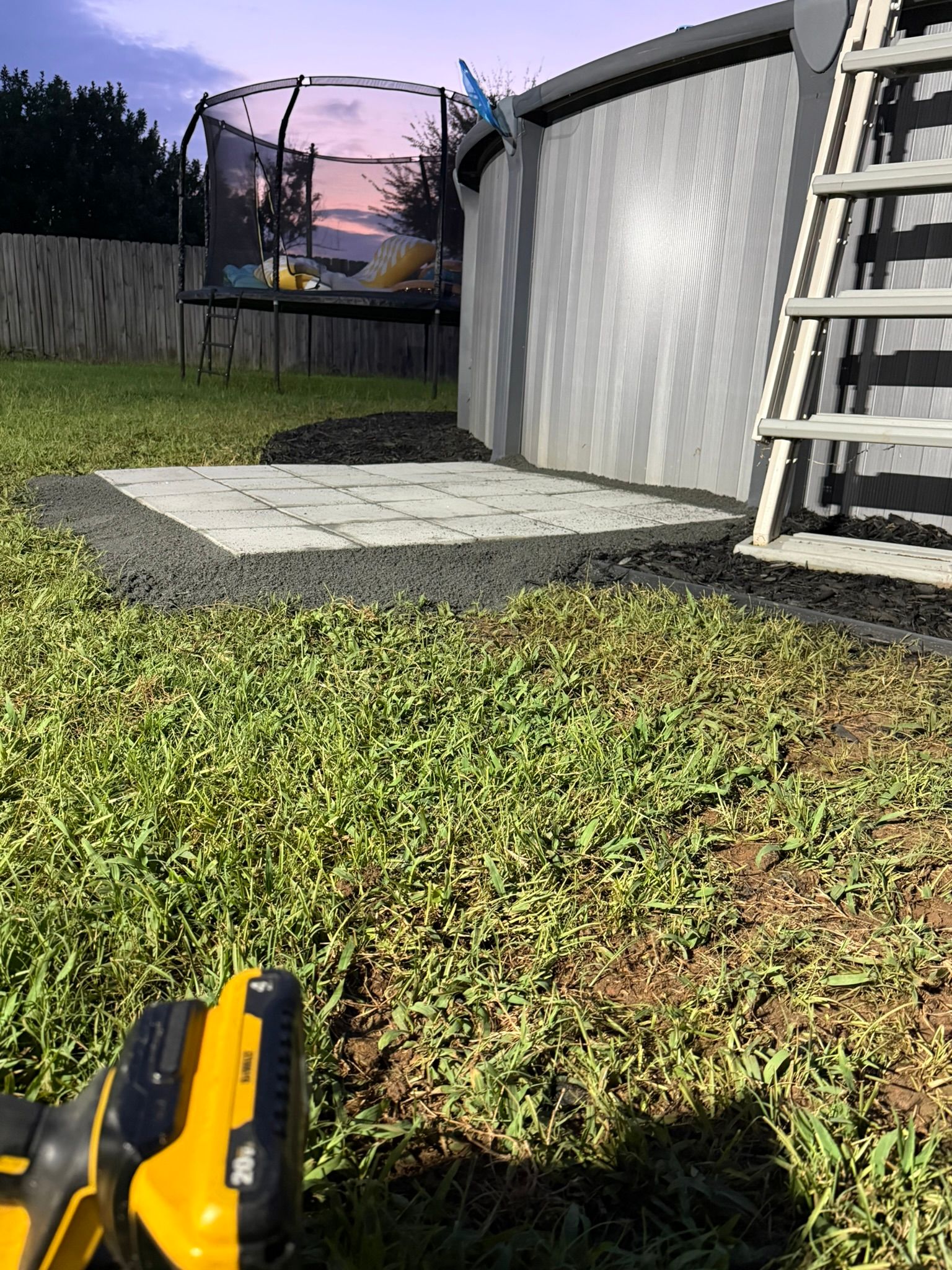 Backyard scene with pool, trampoline, and grass. A ladder leads into the pool; a level tool is in the foreground.