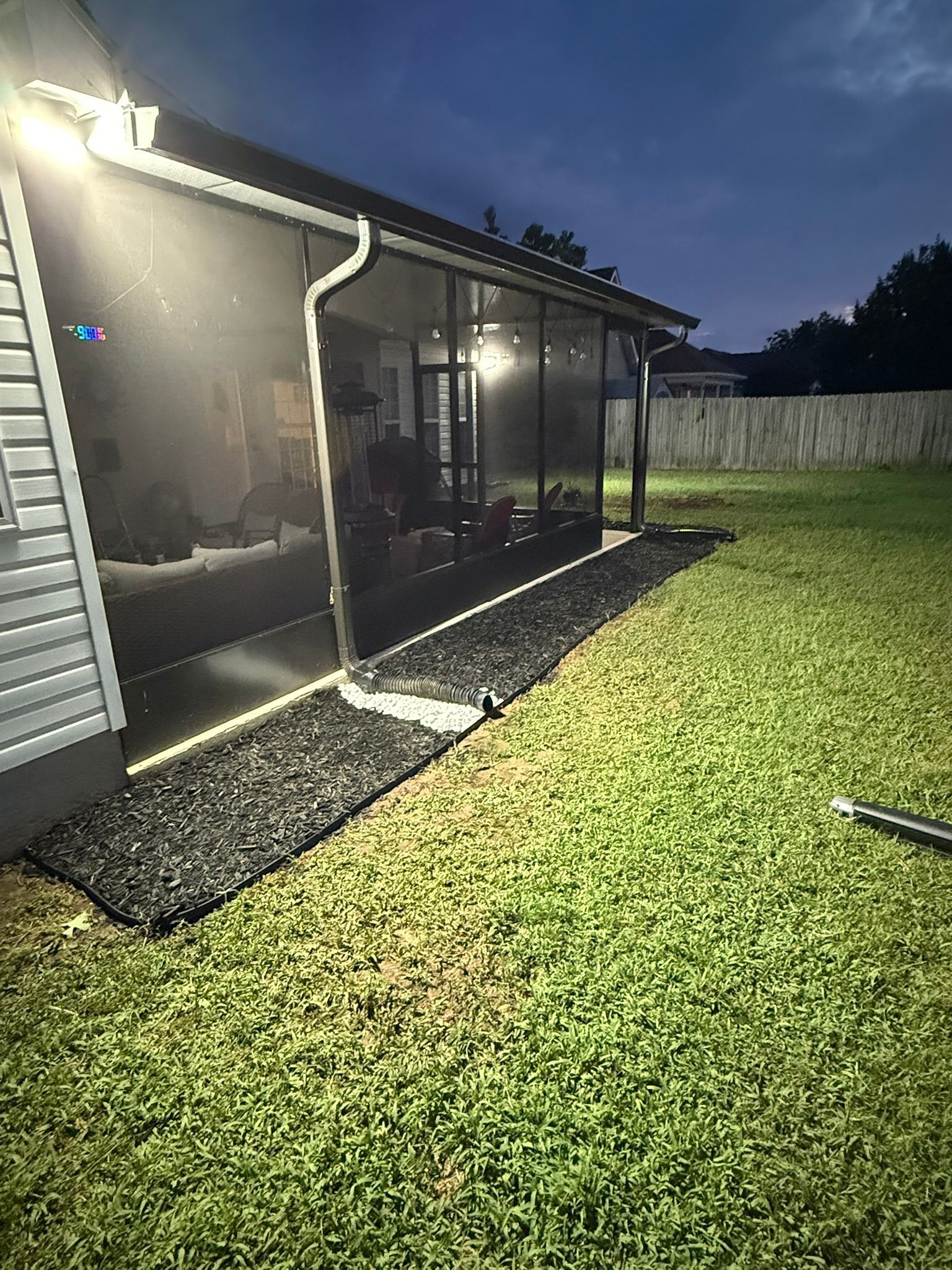 Backyard at night with a screened porch, black mulch bed, and green grass.