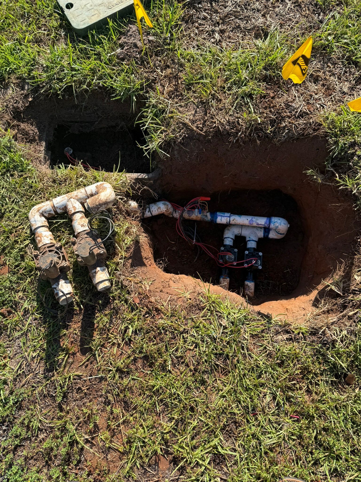 Open irrigation valve box with white PVC pipes and wires in a grassy yard.