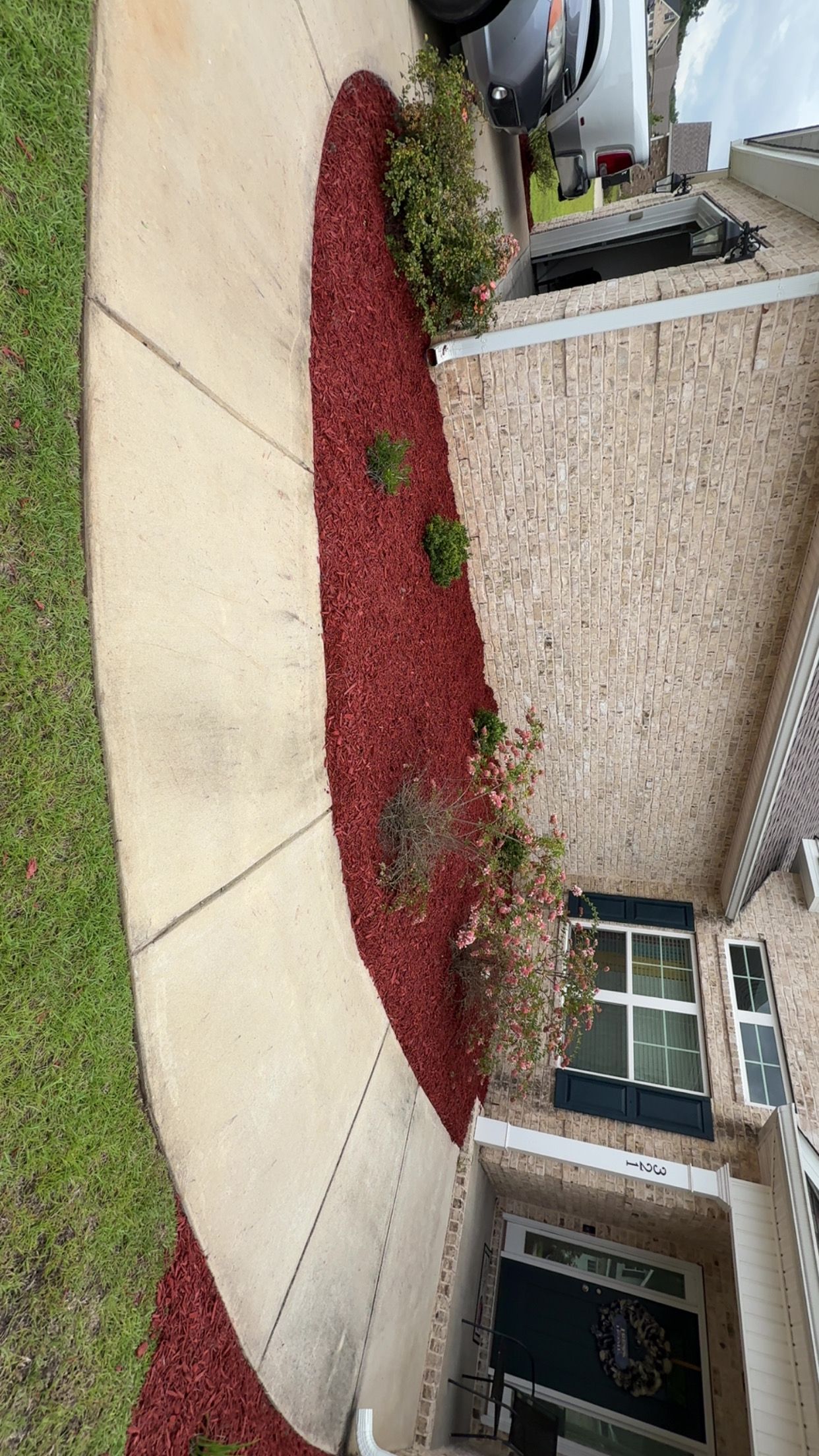 Red mulch bed along curved sidewalk next to a brick house.