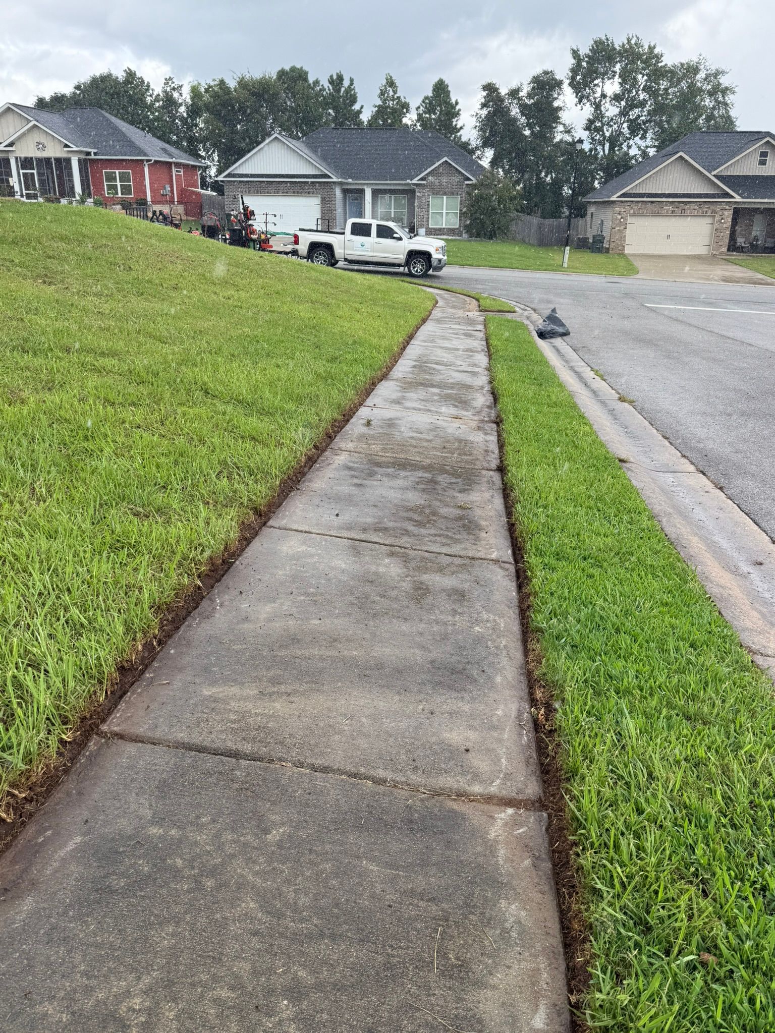 A concrete sidewalk with a fresh grass edge next to a road in a residential neighborhood.