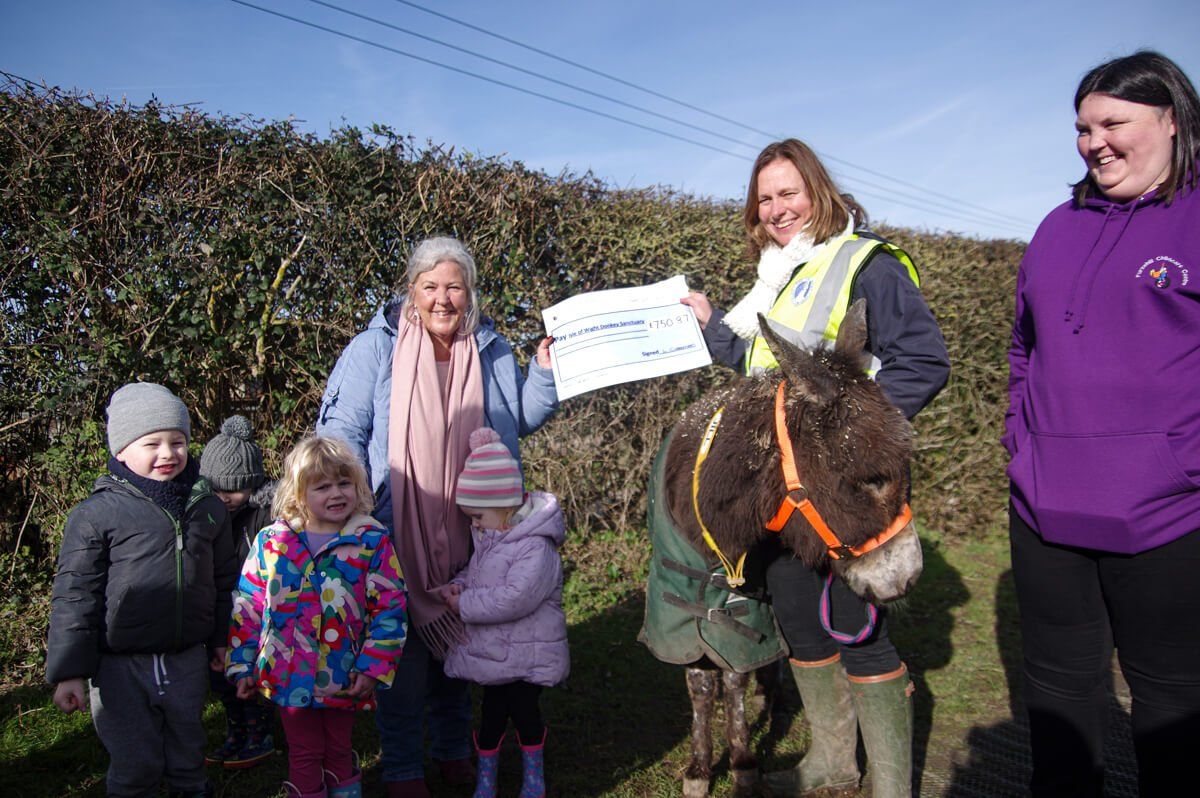 Group of people and children presenting a cheque with a donkey at the Isle of Wight Donkey Sanctuary