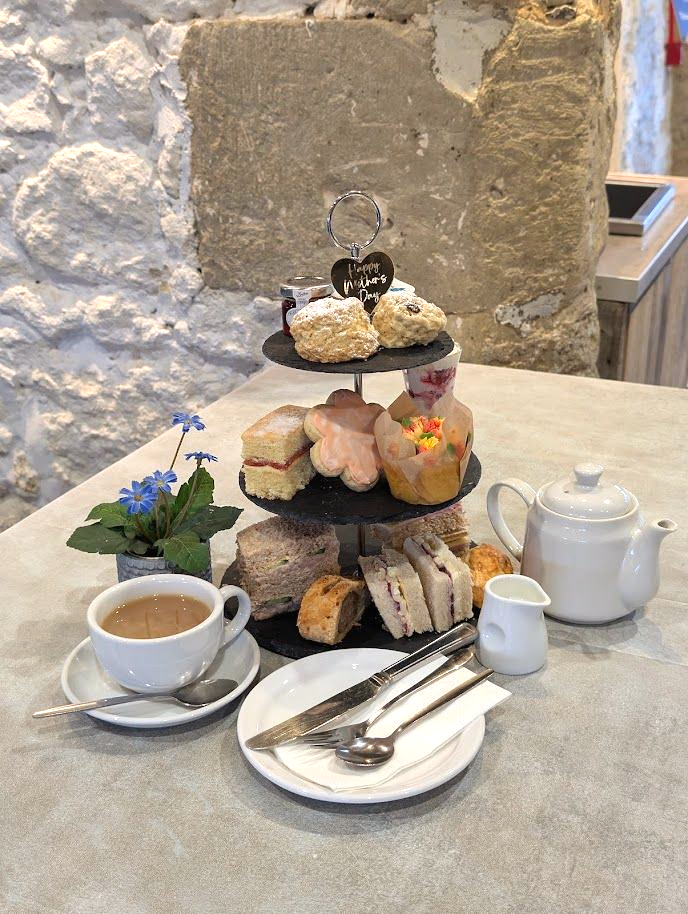 A three tiered stand with cakes, scones and sandwiches on it. 