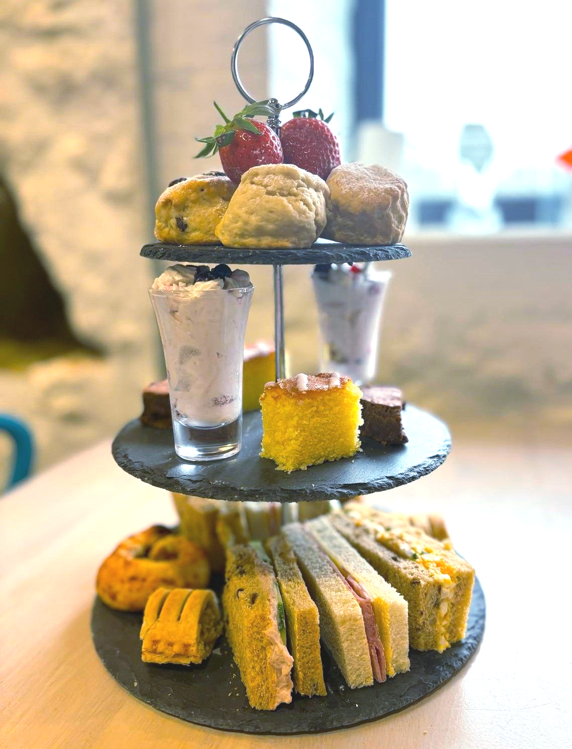 A three tiered stand with cakes, scones and sandwiches on it. 