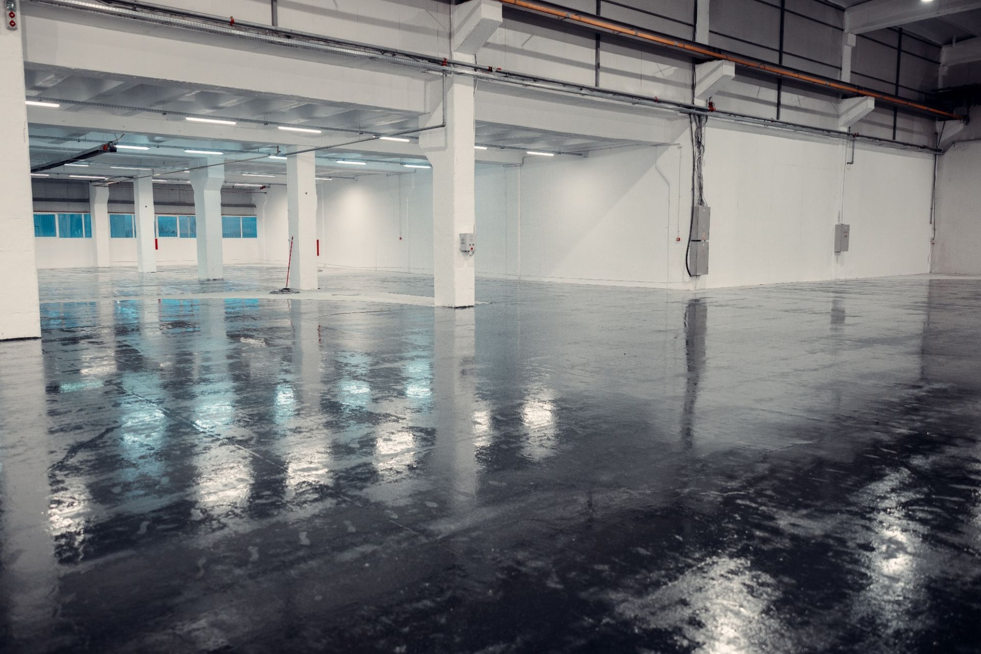 Empty industrial warehouse with glossy, reflective floor and bright white walls.