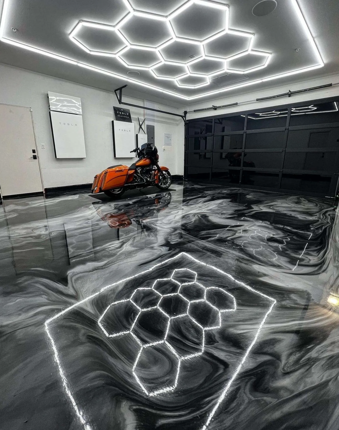 Garage with honeycomb-shaped ceiling lights, black motorcycle, and epoxy flooring with white and gray patterns.