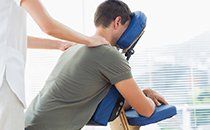 A man is sitting in a chair getting a massage from a woman.