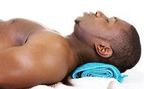 A man is laying on his back with a towel around his neck.