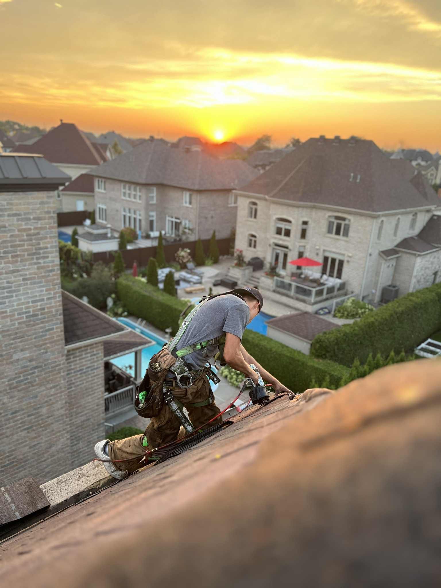 Couvreur sur un toit sombre au lever du soleil, maisons en arrière-plan.