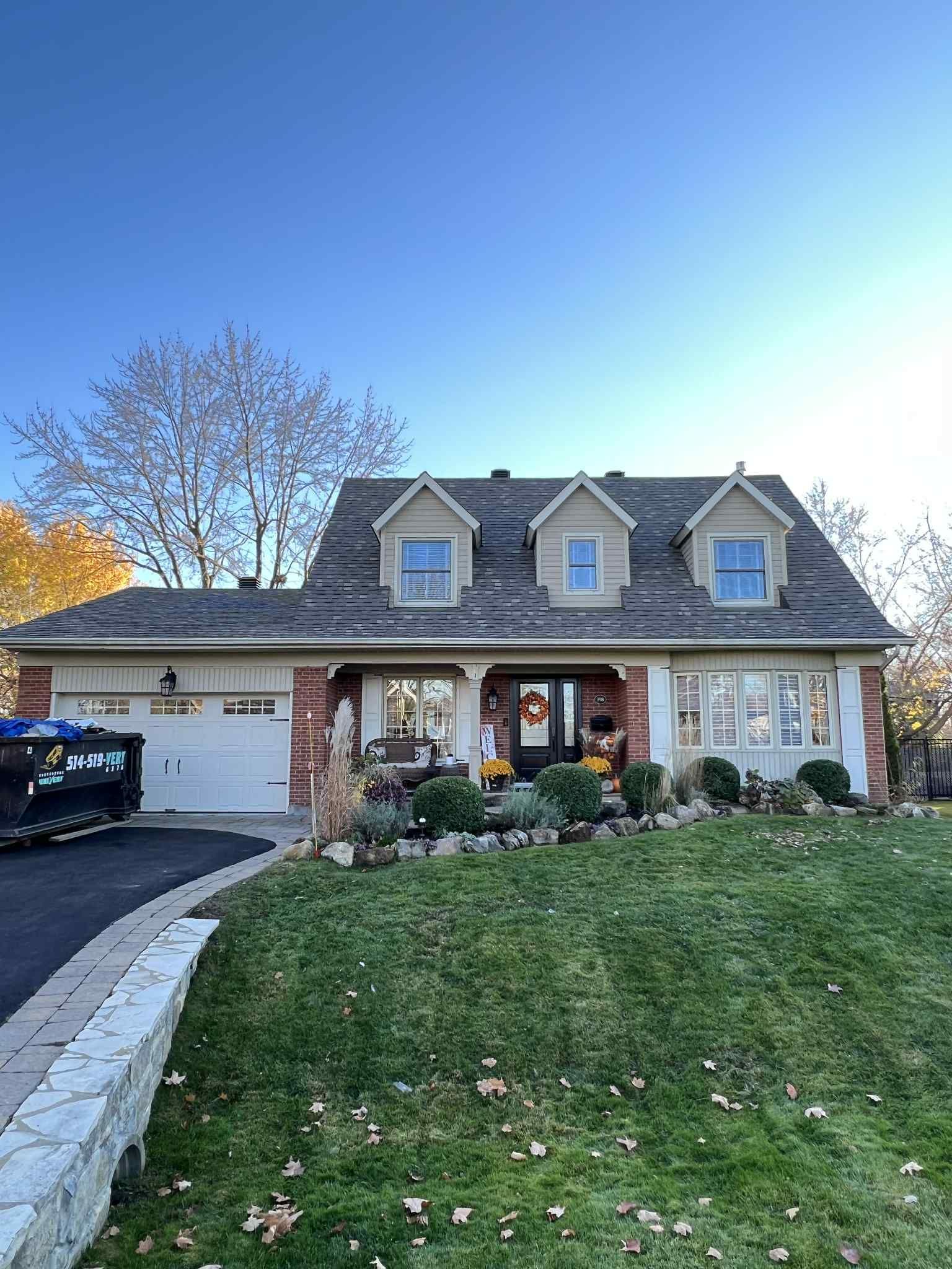 Une maison de banlieue avec un toit sombre et une pelouse bien entretenue sous un ciel bleu.