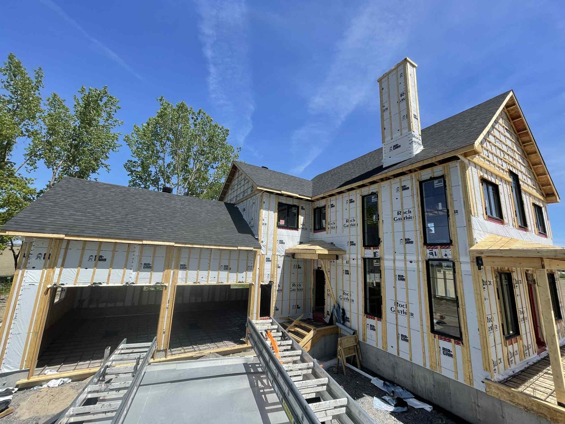 Une maison à deux étages en construction, avec garage, cheminée et ciel bleu.