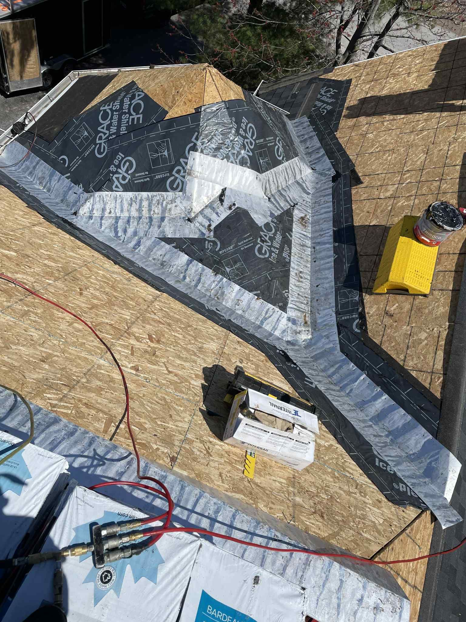 Vue aérienne d'une toiture en construction. Solins métalliques gris et bardeaux sur un platelage en contreplaqué.