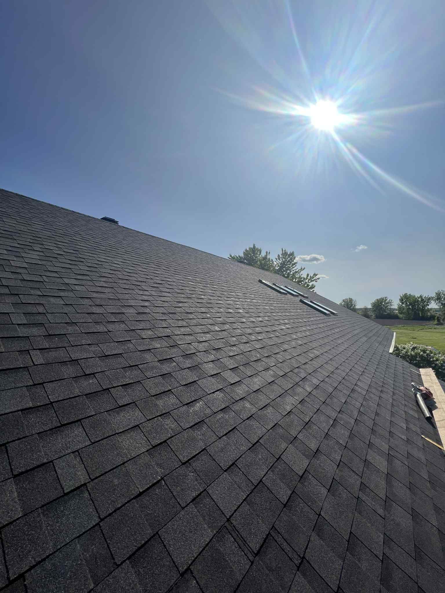 Toit en bardeaux d'asphalte foncé sous un ciel radieux.