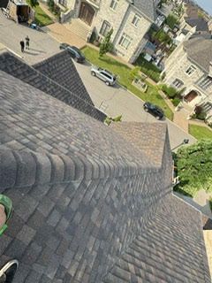 Vue aérienne d'un toit en bardeaux bruns, donnant sur une rue résidentielle et des maisons par une journée ensoleillée.