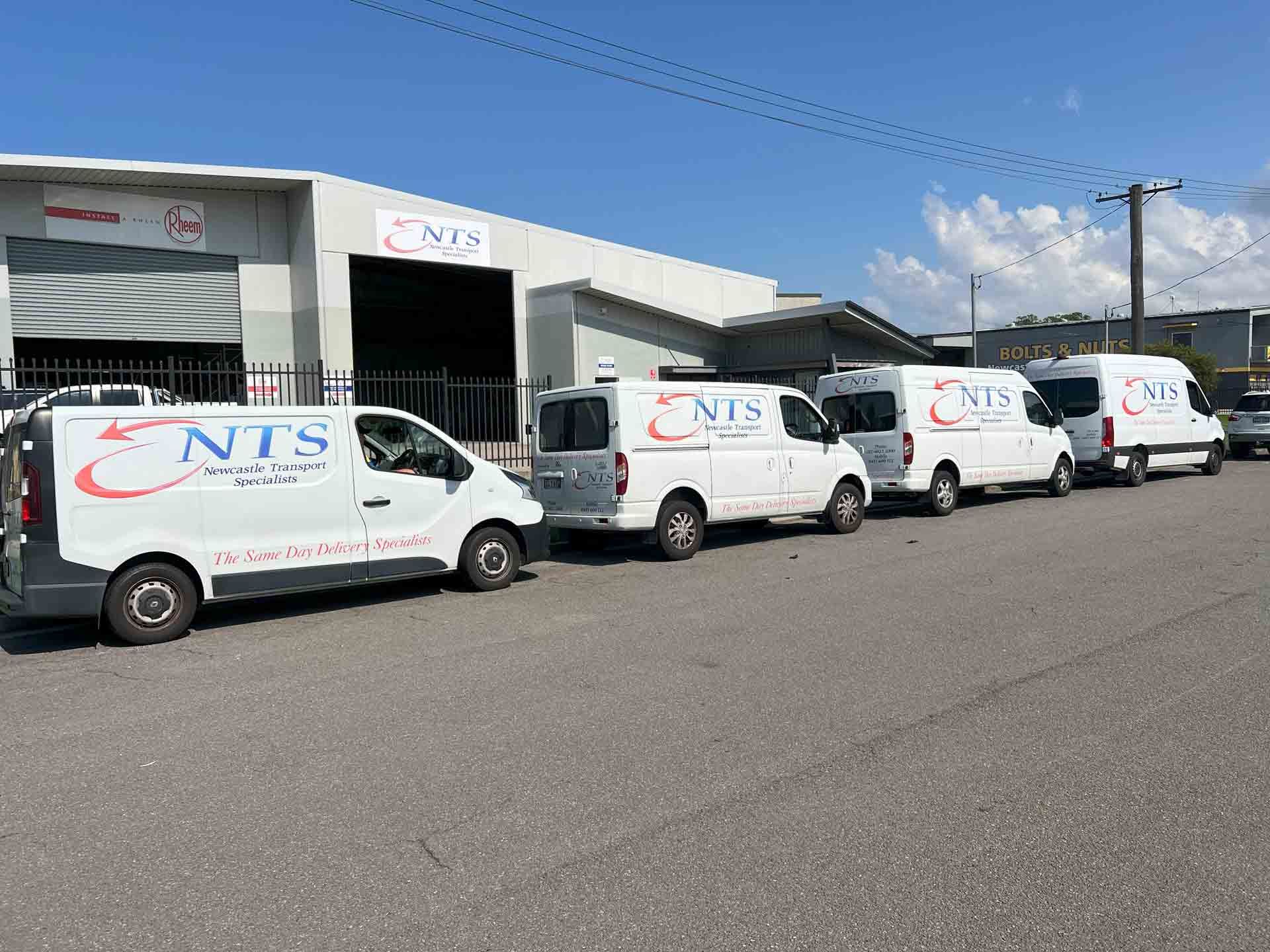 A row of NTS vans are parked in front of a building