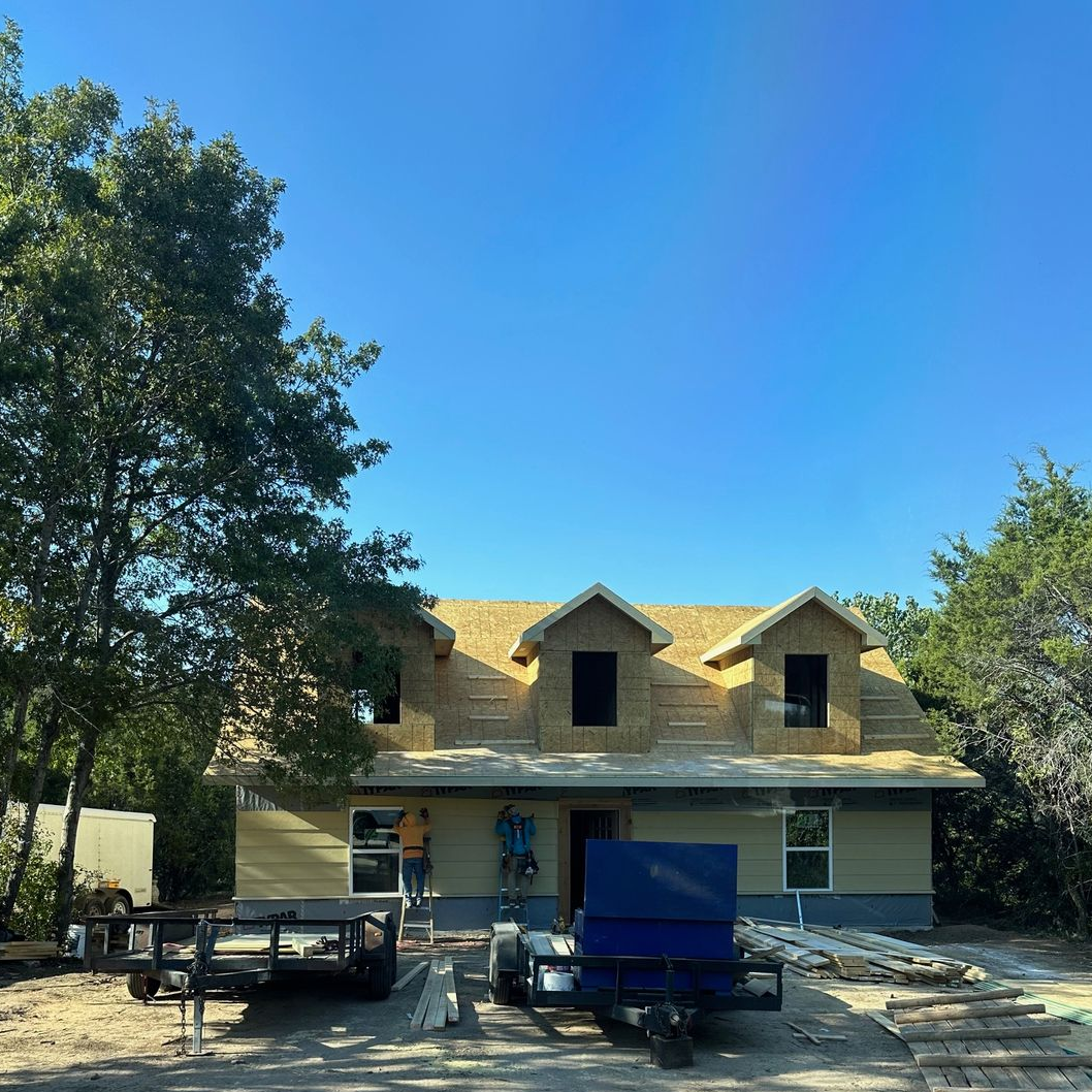 House under construction with framing exposed, blue sky.