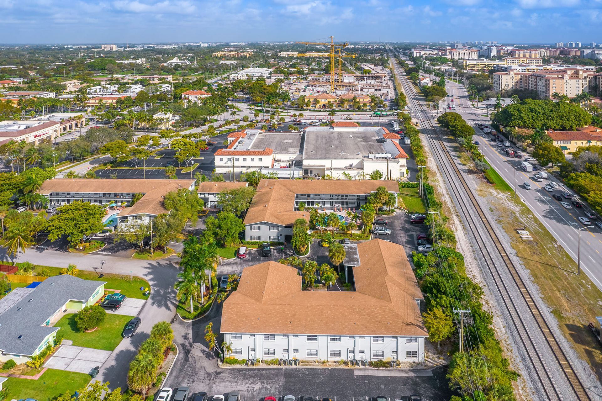 Aerial view of a multifamily complex with tan roofs, trees, and surrounding streets.