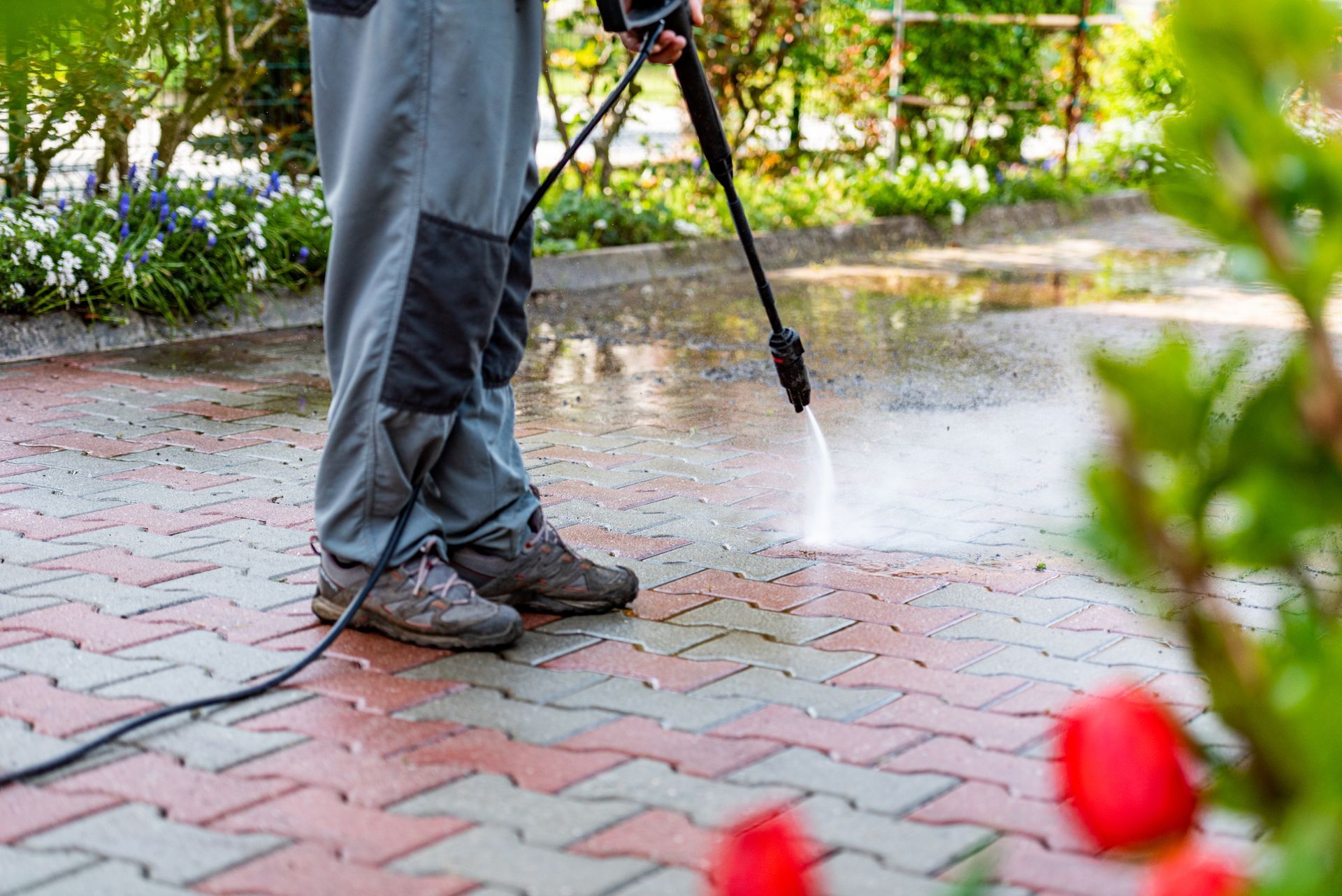 A man is using a high pressure washer to clean a brick sidewalk.