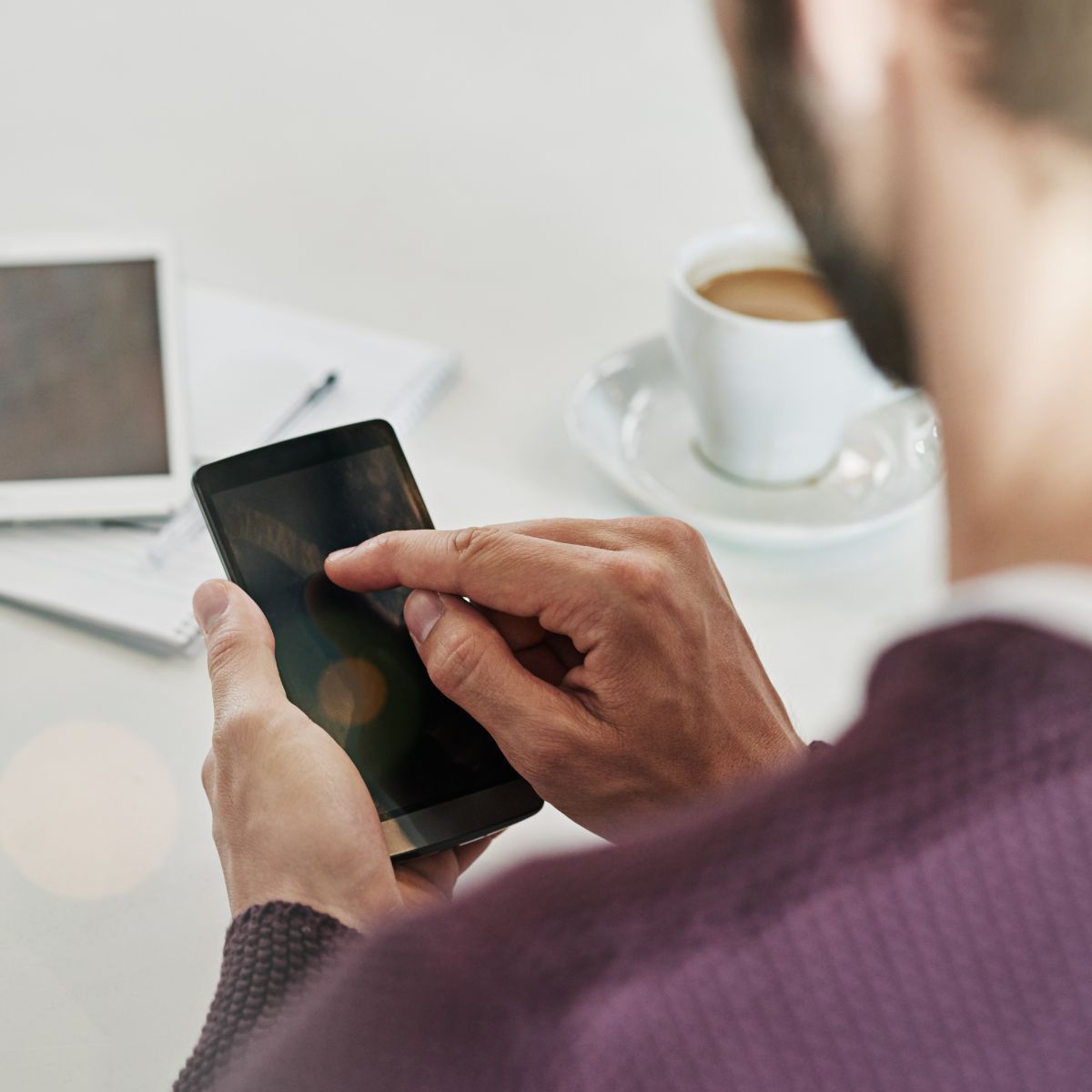 A man in a purple sweater is using a smart phone