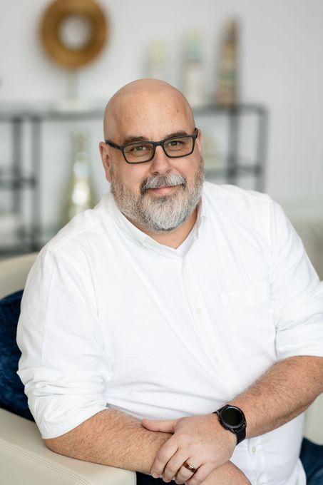 A bald man with a beard and glasses is sitting on a couch.