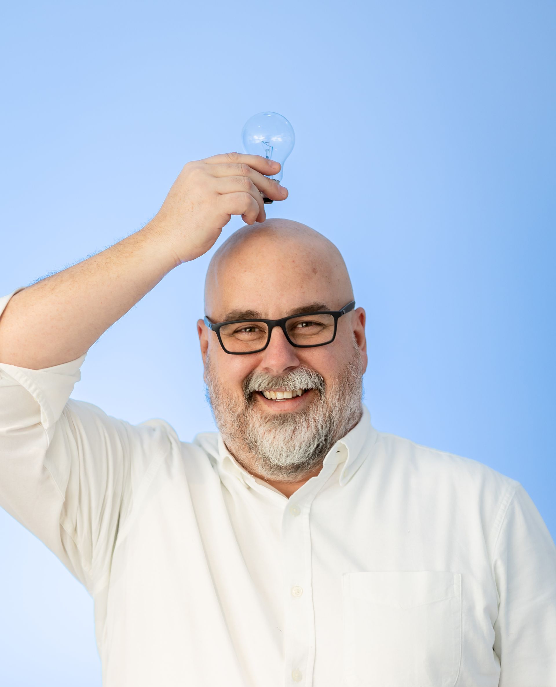 A man with glasses and a beard is holding a light bulb on his head.