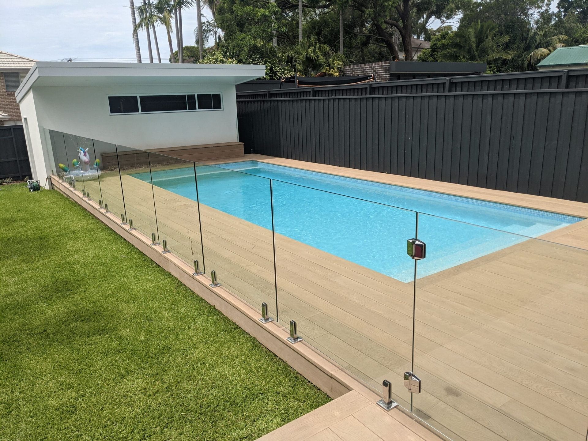 A Swimming Pool Is Surrounded By A Glass Fence In A Backyard — Star Glass Design Pty Ltd in Mayfield, NSW