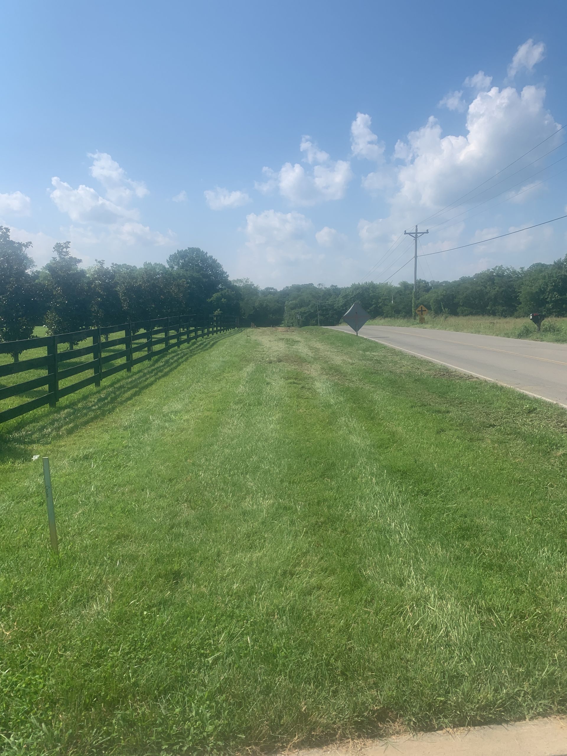 A lush green field with a wooden fence along the side of the road.