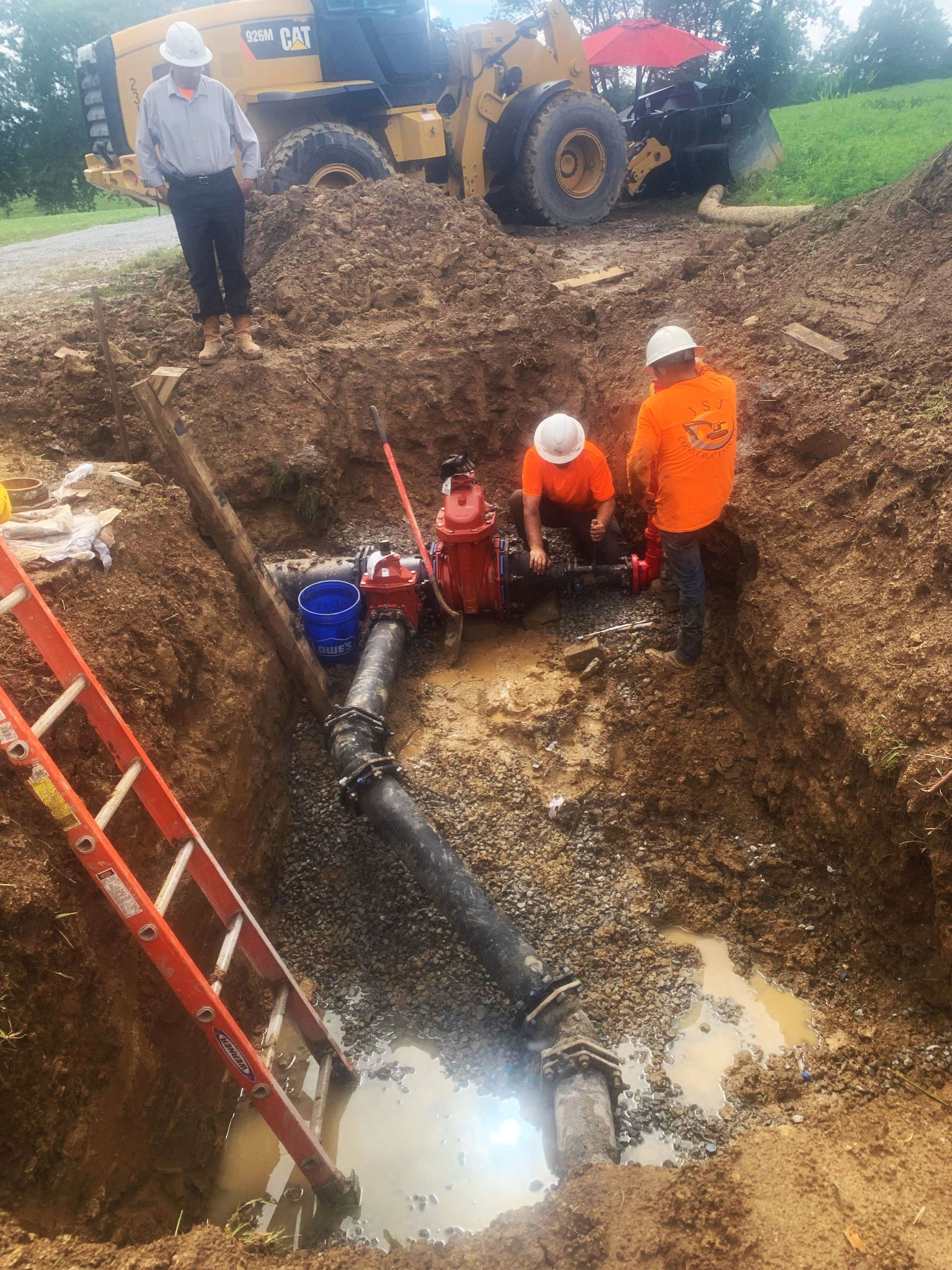 A group of construction workers are working on a pipe in the dirt.