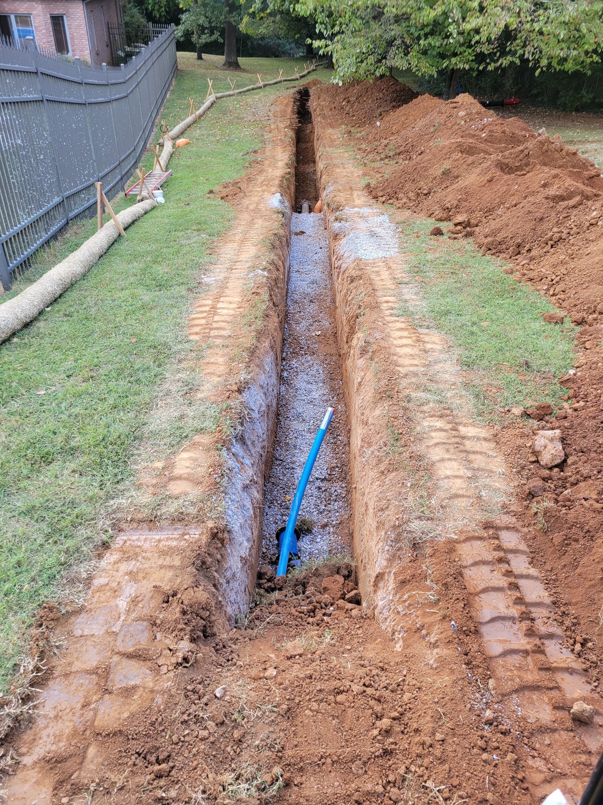 A blue pipe is being installed in a trench in a yard.