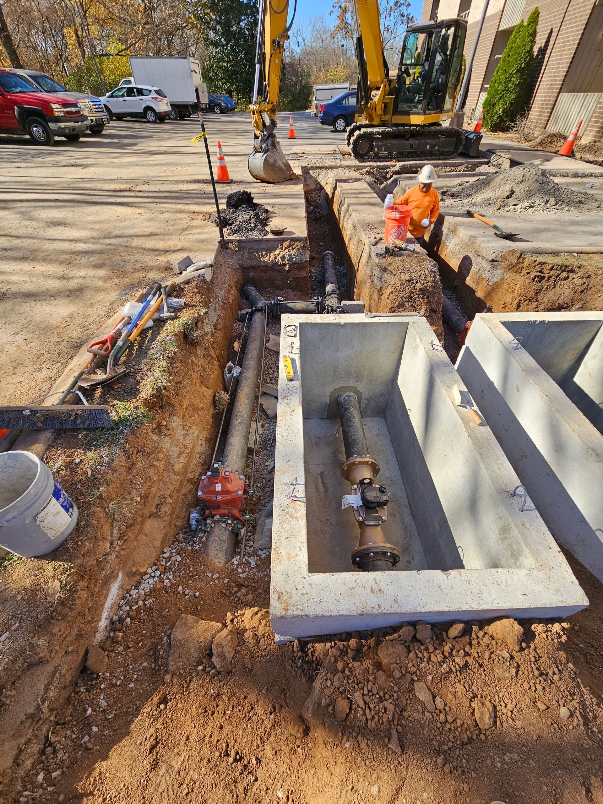 A man is sitting in a trench next to a yellow excavator.