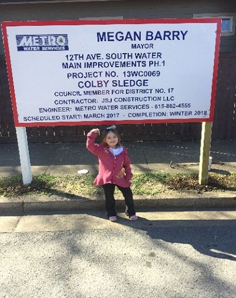 A little girl is standing in front of a megan barry sign