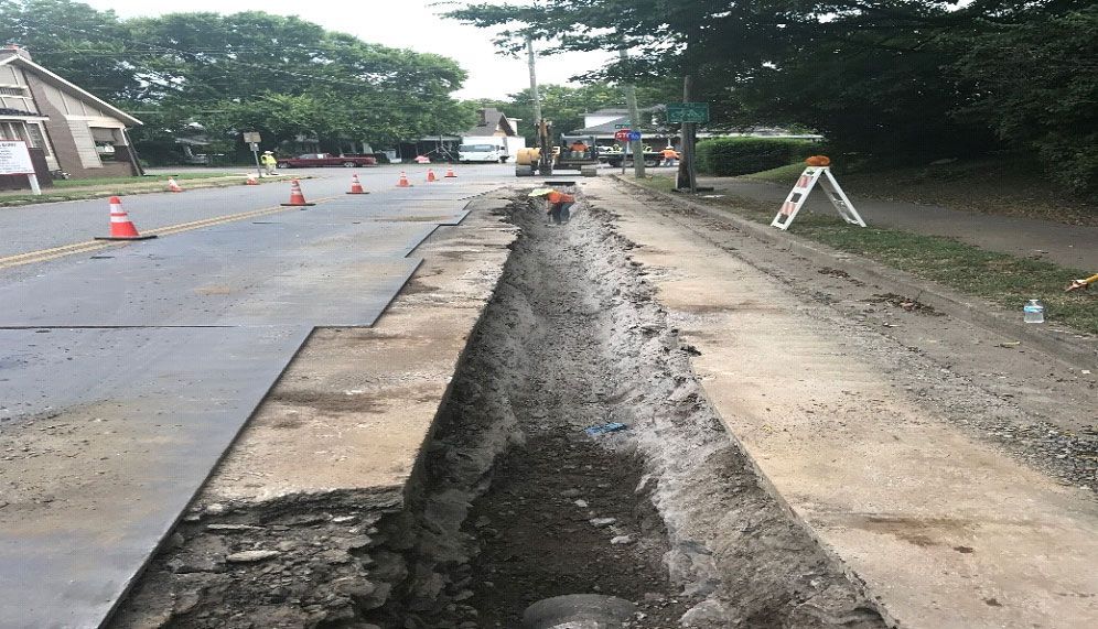 A large hole in the side of a road is being filled with dirt.