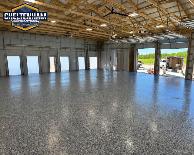 Large workshop with a polished gray speckled epoxy floor, wooden ceiling trusses, and open garage doors.