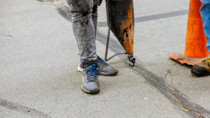 A person is standing on the side of the road holding a tool.