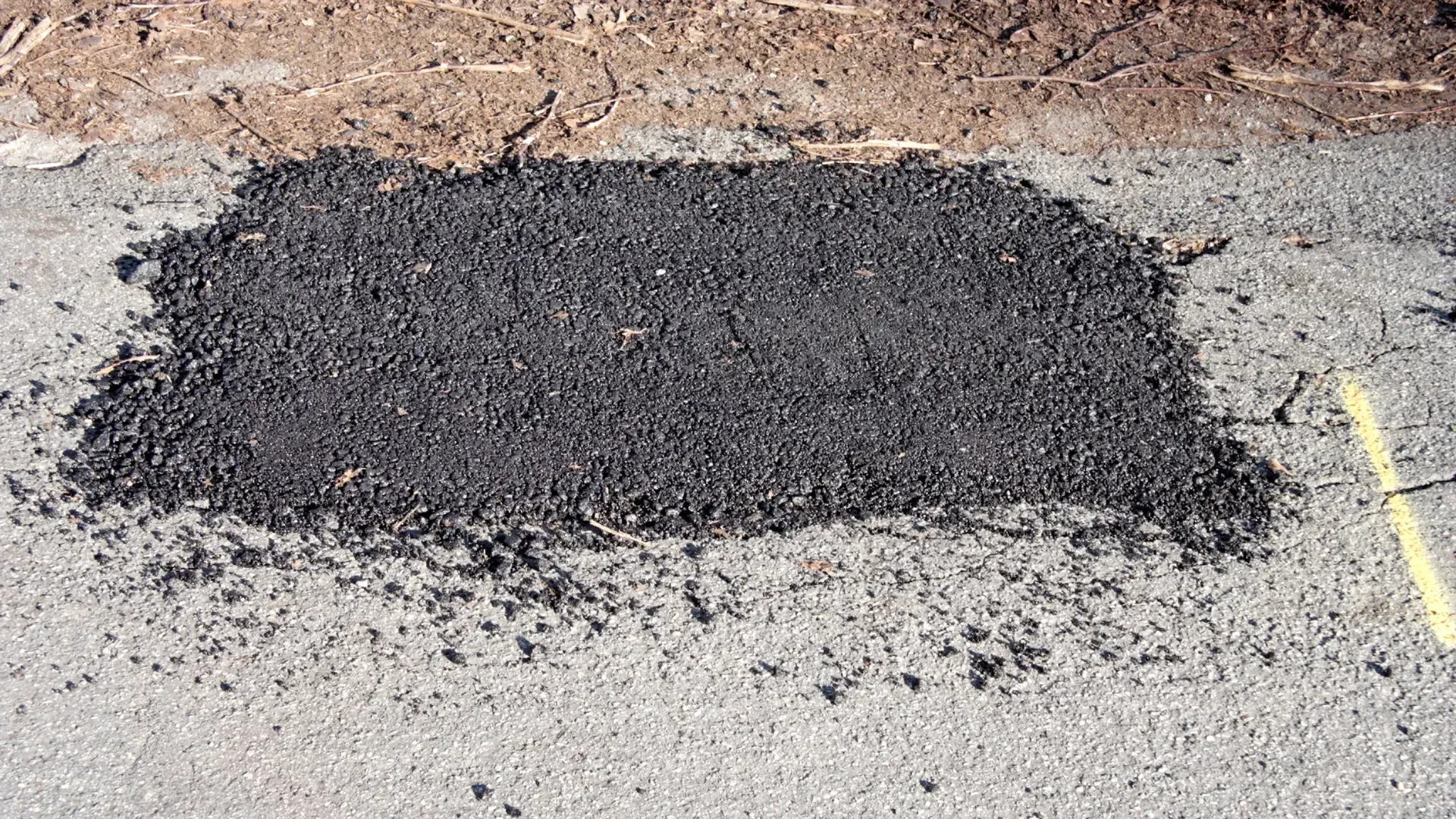A patch of asphalt is sitting on the ground next to a yellow line.
