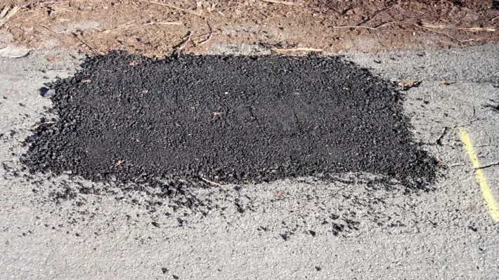 A patch of asphalt is sitting on the ground next to a yellow line.