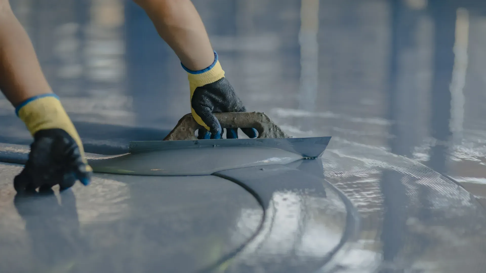 A person is using a trowel to spread concrete on a floor.