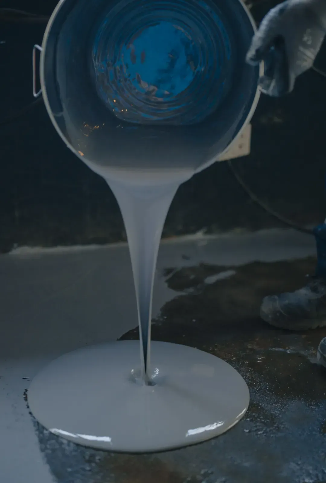 A person is pouring white paint into a bucket.