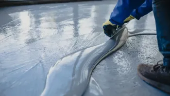 A person is spreading a liquid on a concrete floor.