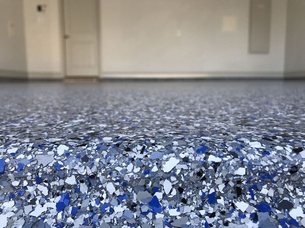 A close up of a garage floor with blue , gray and white flakes.