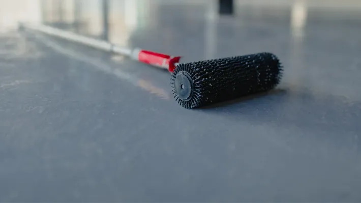 A paint roller is sitting on a concrete floor.