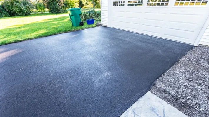 A black asphalt driveway next to a white garage door.