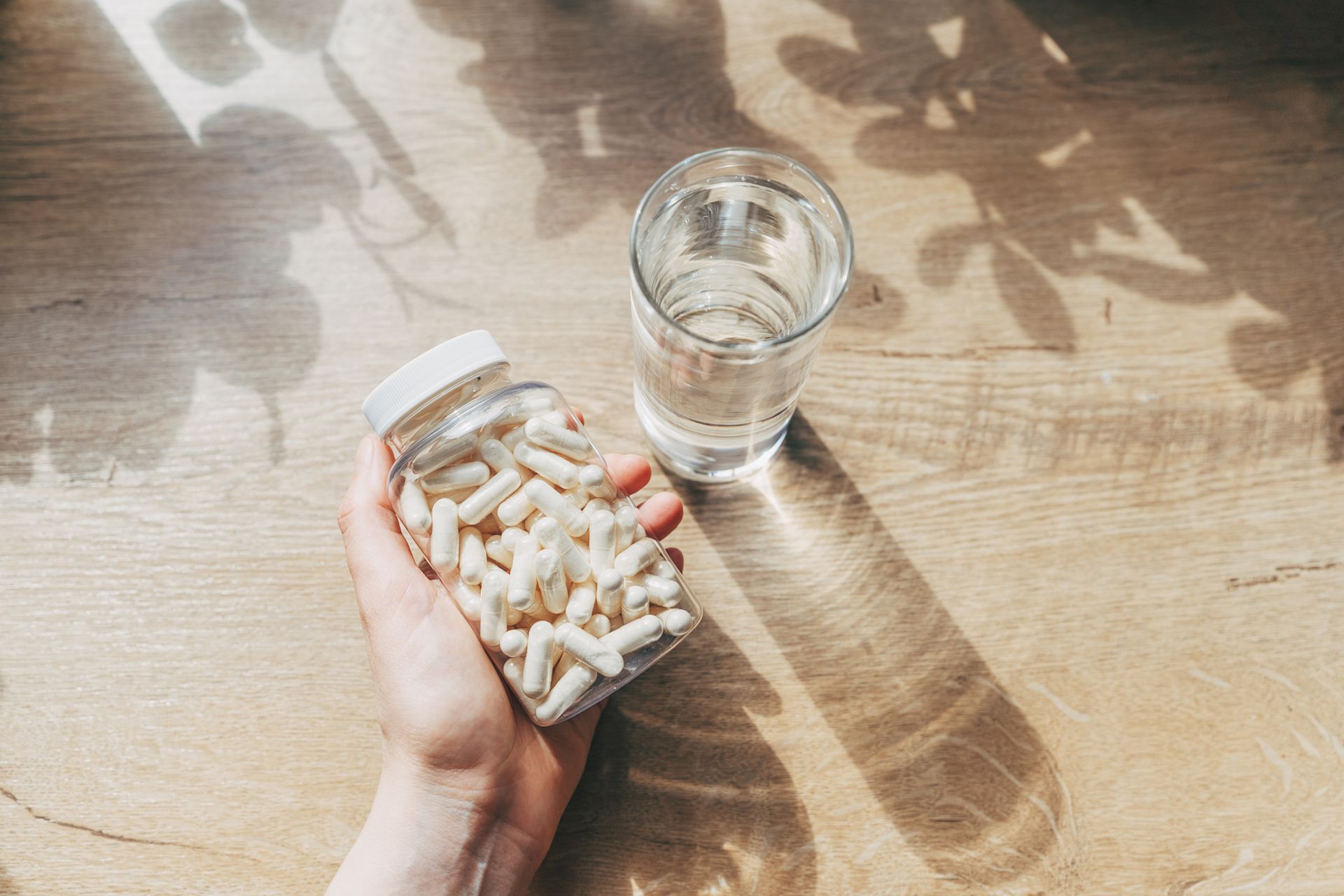 A person is holding a bottle of pills and a glass of water.