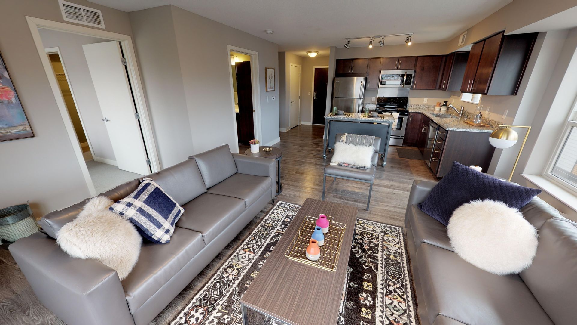 Apartment living room and kitchen with couches, an island, brown cabinetry, and stainless steel appliances