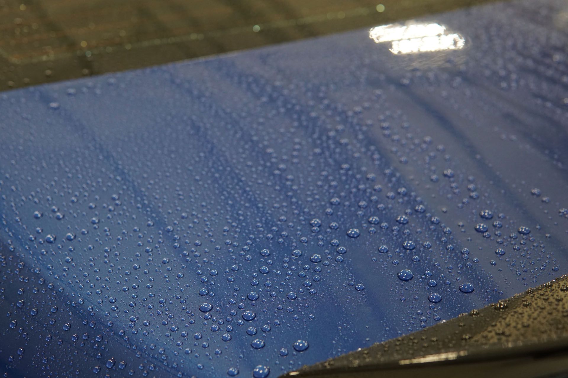 A close up of a blue car with water drops on it.